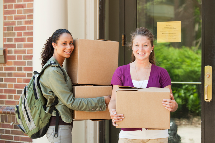 Subject: Two University students in front of their dorm moving boxes in a college campus.