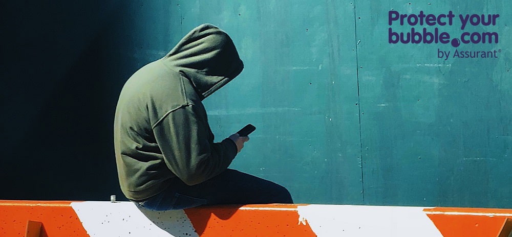 Man sitting on a barrier with a mobile phone in a hoodie
